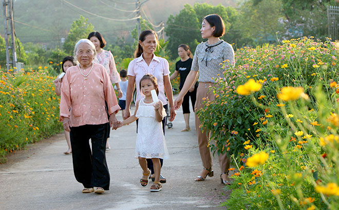 Bà con nhân dân đi trên tuyến đường hoa rực rỡ ở Đại Minh - xã nông thôn mới kiểu mẫu đầu tiên của huyện Yên Bình, năm 2023 (Ảnh: T.L)